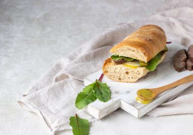 Beyaz ahşap kesme tahtası üzerinde soğan ve cukes ve Hardal soslu etli sandviç taze salata, kızartma