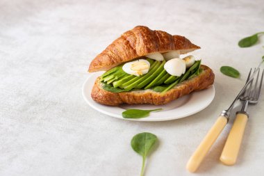 Kruvasan yeşil salata, avokado ve ışık gri arka plan üzerinde yumurta. Kahvaltı, brunch veya öğle yemeği kavramı.