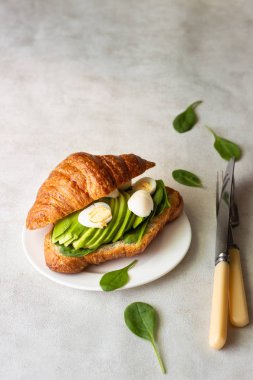 Kruvasan yeşil salata, avokado ve ışık gri arka plan üzerinde yumurta. Kahvaltı, brunch veya öğle yemeği kavramı.