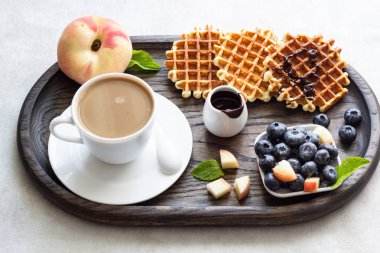 Taze yaban mersini, şeftali, çikolata sosu ve bir fincan kahve bir rustik ahşap kesme tahtası üzerinde Belçika Waffle. Liege stil Belçika Waffle. Kahvaltı ve öğle yemeği kavramı.