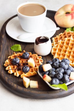 Taze yaban mersini, şeftali, çikolata sosu ve bir fincan kahve bir rustik ahşap kesme tahtası üzerinde Belçika Waffle. Liege stil Belçika Waffle. Kahvaltı ve öğle yemeği kavramı.