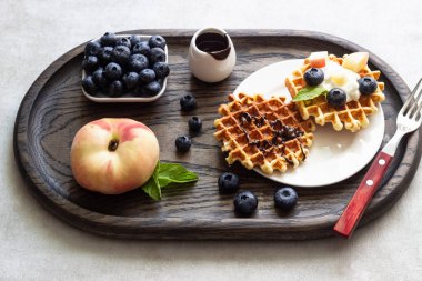 Taze yaban mersini, şeftali ve rustik ahşap kesme tahtası üzerine çikolata sosu ile Belçika Waffle. Liege stil Belçika Waffle. Kahvaltı ve öğle yemeği kavramı.