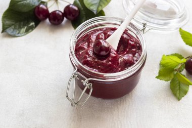 Ev yapımı kiraz reçel kavanoz ile hafif bir arka plan üzerinde taze kiraz.