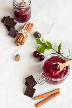 Ev yapımı kiraz reçeli ile çikolata, hafif bir arka plan üzerinde bir kavanoza taze kiraz ile baharat (tarçın, Hindistan cevizi).