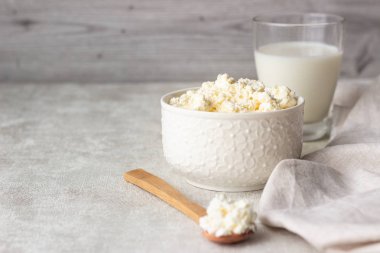 Bir kaşık hafif bir arka plan üzerinde beyaz bir seramik kase taze tarım süzme peynir. Süt ve süt ürünleri. Seçici odak. Kopya alanı