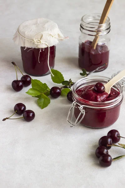 Homemade cherry jam in jars with fresh cherries on a light background.
