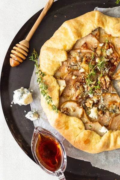 Homemade rustic galette with pears, blue cheese, walnuts and honey on light background. Gallette with a buttery crust and sweet fruit filling. Rustic style.