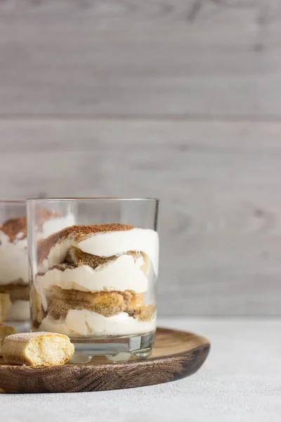 Traditional Italian dessert tiramisu in glass on light grey background. Coffee flavored Italian dessert made of ladyfingers and mascarpone.