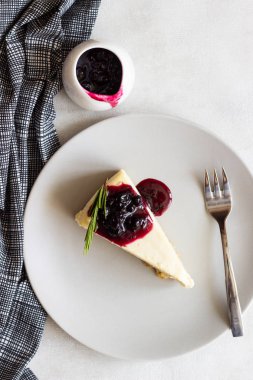 New York tarzı cheesecake siyah frenk üzümü sos ve biberiye ışık arka plan üzerinde gri plaka üzerinde parça.