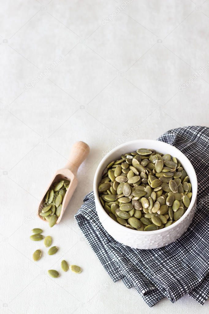 Bowl of raw pumpkin seeds on a light grey background. Copy space. 