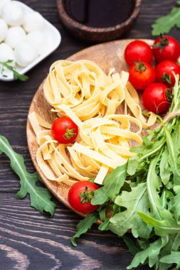 Makarna yemek pişirmek için malzemeler. Tagliatelle, cherry domates, roka, zeytin yağı ve mozzarella eski ahşap zemin üzerinde. İtalyan pasta malzemeler.