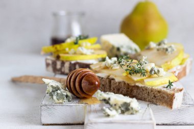Tost veya bruschetta ricotta veya krem peynir, armut, bal ve beyaz tahta kesme tahtası üzerinde mavi peynir ile. Lezzetli kahvaltı veya aperatif hafif bir arka plan üzerinde.