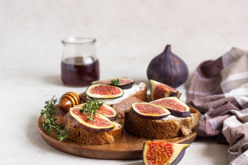 Mini bruschetta (toast or sandwich) with ricotta (cream cheese), fig, honey and thyme served on wooden rustic plate. Healthy food concept. 