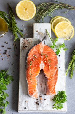 Aromatik otlar, zeytinyağı, limon, tuz ve biber gri beton zemin üzerine taze çiğ somon steak kısmı. Sağlıklı gıda, diyet veya pişirme kavramı.