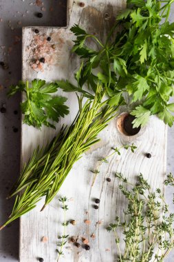 Kekik, biberiye, maydanoz, tuz ve biber bir beyaz tahta kesme tahtası üzerinde. Bahçe ve baharat kokulu otlar.