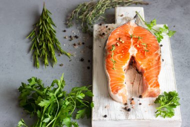 Aromatik otlar (biberiye, kekik, maydanoz), tuz ve biber hafif ahşap kesme tahtası üzerinde taze çiğ somon steak kısmı. Sağlıklı gıda, diyet veya pişirme kavramı.