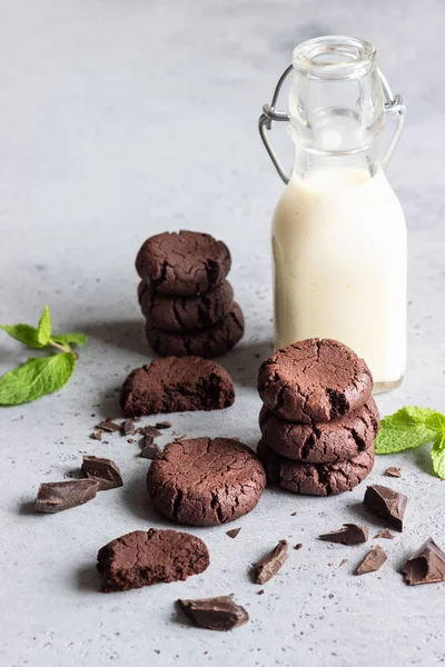 Chocolate cookies with pieces of chocolate and mint with milk on a grey concrete background.