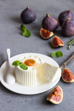 Ricotta peyniri incir, tatlım, nane ve kekik gri beton zemin üzerine beyaz tabakta. Metin için yer kopyalayın.
