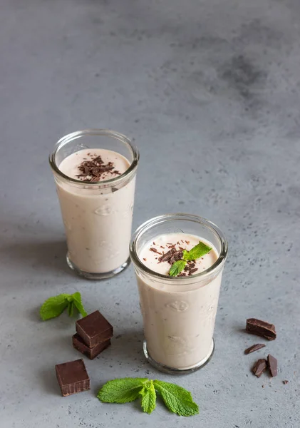 Delicious chocolate drink (milkshake, cocktail or smoothie) in glasses with pieces of chocolate on grey concrete background.