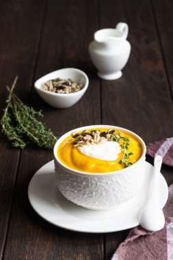 Krem, tohum ve kekik eski ahşap arka plan üzerinde beyaz bir seramik kase ile kalın balkabağı çorbası. Kopya alanı