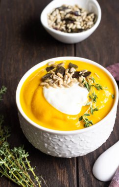 Krem, tohum ve kekik eski ahşap arka plan üzerinde beyaz bir seramik kase ile kalın balkabağı çorbası. Kopya alanı