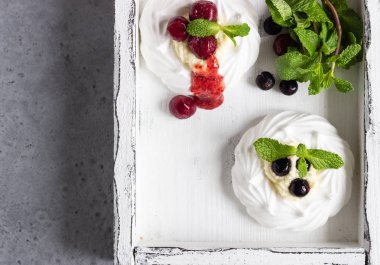 Mini Pavlova veya beze yuva ile krem şanti, çilek ve nane, seçici odak. Gri beton arka plan. Kopya alanı.