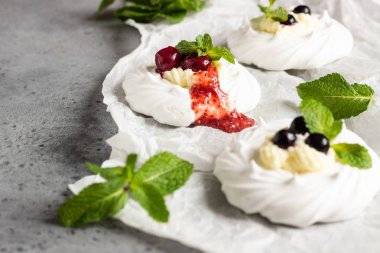 Mini Pavlova veya beze yuva ile krem şanti, çilek ve nane, seçici odak. Gri beton arka plan. Kopya alanı.