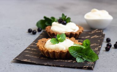 Mini tart (tartlets) ile krem şanti veya muhallebi ve taze çilek nane ile servis. Ev yapımı tatlılar. Gri arka plan. Kopya alanı.