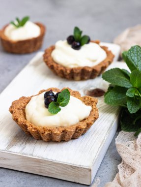 Mini tart (tartlets) ile krem şanti veya muhallebi ve taze çilek nane ile servis. Ev yapımı tatlılar. Gri arka plan. Kopya alanı.