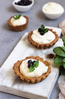 Mini tart (tartlets) ile krem şanti veya muhallebi ve taze çilek nane ile servis. Ev yapımı tatlılar. Gri arka plan. Kopya alanı.