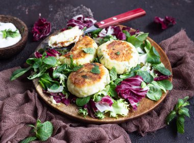 Cottage cheese pancakes or syrniki with cheese, green onion, dill and parsley served with salad mix and sour cream with mint.