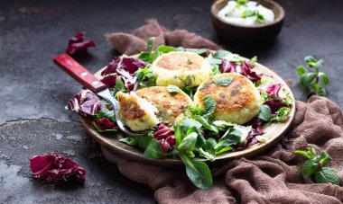 Cottage cheese pancakes or syrniki with cheese, green onion, dill and parsley served with salad mix and sour cream with mint.