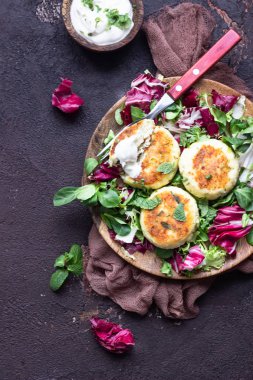 Cottage cheese pancakes or syrniki with cheese, green onion, dill and parsley served with salad mix and sour cream with mint.