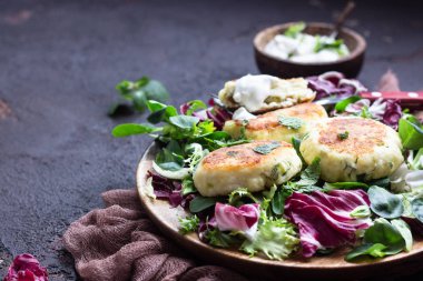 Cottage cheese pancakes or syrniki with cheese, green onion, dill and parsley served with salad mix and sour cream with mint.