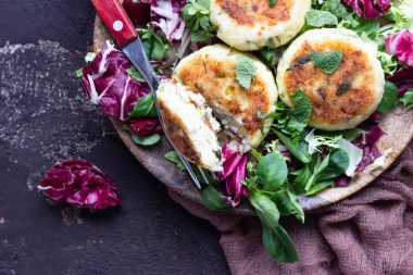 Cottage cheese pancakes or syrniki with cheese, green onion, dill and parsley served with salad mix and sour cream with mint.