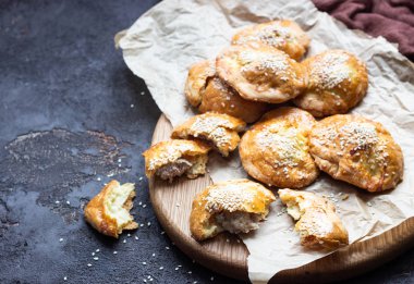 Taze et mini pies eski koyu kahverengi zemin, rustik tarzı bir kağıt üzerinde. Taze pişmiş pasties et (tavuk veya hindi) ile dolu. Kopya alanı.