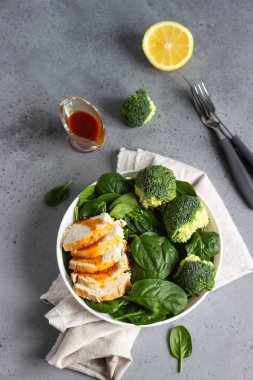 Ispanak, brokoli ve beyaz tabakta narenciye sosu ile tavuk göğsü. Gri beton arka plan. Uzay kopyalayın. Sağlıklı Diyet öğle veya akşam yemeği. Keto diyet.