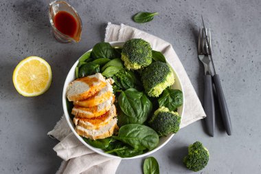 Ispanak, brokoli ve beyaz tabakta narenciye sosu ile tavuk göğsü. Gri beton arka plan. Uzay kopyalayın. Sağlıklı Diyet öğle veya akşam yemeği. Keto diyet.