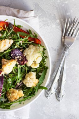 Roka, kavrulmuş sebze (karnabahar, kırmızı biber ve soğan) ve tohum salatası. Sağlıklı gıda. Açık gri beton renkli. Kopya alanı.