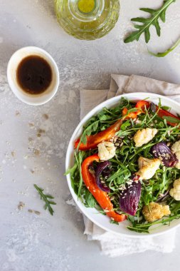 Roka, kavrulmuş sebze (karnabahar, kırmızı biber ve soğan) ve tohum salatası. Sağlıklı gıda. Açık gri beton renkli. Kopya alanı.