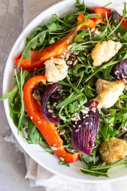 Roka, kavrulmuş sebze (karnabahar, kırmızı biber ve soğan) ve tohum salatası. Sağlıklı gıda. Açık gri beton renkli. Kopya alanı.