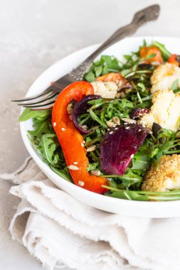 Roka, kavrulmuş sebze (karnabahar, kırmızı biber ve soğan) ve tohum salatası. Sağlıklı gıda. Açık gri beton renkli. Kopya alanı.