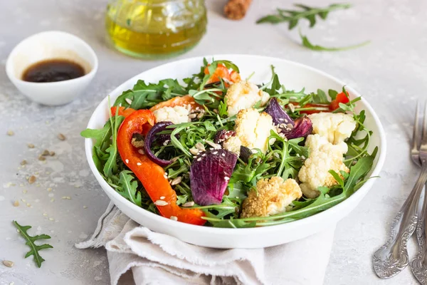 Roka, kavrulmuş sebze (karnabahar, kırmızı biber ve soğan) ve tohum salatası. Sağlıklı gıda. Açık gri beton renkli. Kopya alanı.