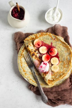 Vanilya haşhaş tohumu krep veya doğal yoğurt, muz ve vişne sosu ile baharat (tarçın ve anason) ile krep. Hafif beton arka plan. Kopya alanı.
