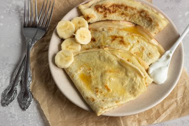 İnce krep veya doğal yoğurt, bal ve muz bir plaka ile krep. Hafif beton arka plan. Kopya alanı.