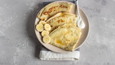 İnce krep veya doğal yoğurt, bal ve muz bir plaka ile krep. Hafif beton arka plan. Kopya alanı.