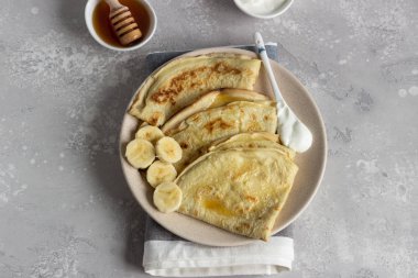 İnce krep veya doğal yoğurt, bal ve muz bir plaka ile krep. Hafif beton arka plan. Kopya alanı.