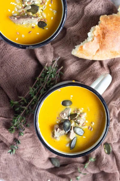 Two portions of fresh homemade pumpkin creamy soup served with liver and seeds in a white enamel mugs on a light grey concrete background. View from above, flat lay. — Stock Image Two Portions Fresh Homemade Pumpkin Creamy Soup Served Liver Seeds Stock Photo