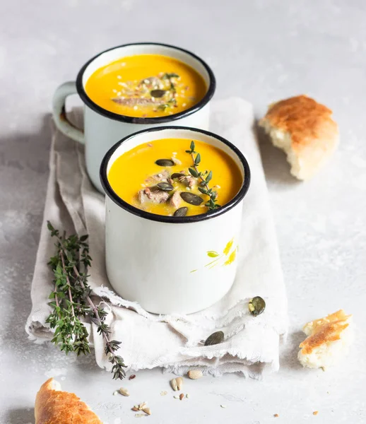 Two portions of fresh homemade pumpkin creamy soup served with liver and seeds in a white enamel mugs on a light grey concrete background. View from above, flat lay. — Stock Image Two Portions Fresh Homemade Pumpkin Creamy Soup Served Liver Seeds Stock Picture