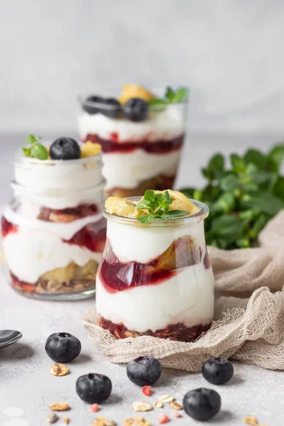 Granola, blueberry and banana greek yogurt parfaits in mason jars. Healthy breakfast. A light grey concrete background. Copy space.
